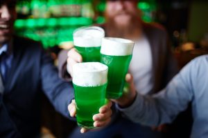 People holding up glasses with green beer