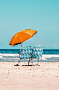 two blue beach chairs on the sand with an orange umbrella