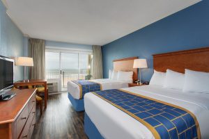 Two double beds in a hotel room with an oceanfront balcony.